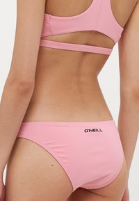 Růžové spodní část plavek bikini s elegantním designem, který nabízí minimální pokrytí, hladkou texturu a černé logo "O'Neill" na zadní straně.