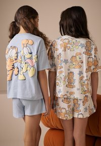 Lys blå kortærmet skjorte og shorts med tegneserie kat- og hundedesign; cremefarvet skjorte og shorts med gentagne farverige karaktermønstre.