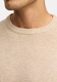 Jersey de punto beige con cuello redondo acanalado, que muestra un patrón texturizado y una tela suave, diseñado para un uso cómodo.