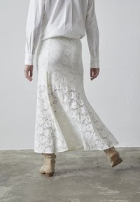 Hvid blonde maxiskørt med en flagrende design, der har en sideslids og indviklede blomster mønstre. Båret med en langærmet hvid skjorte og beige støvler.