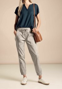 Lösa grå byxor med elastiska mudd, kombinerat med en mörk teal V-ringad topp. Tillbehör inkluderar en brun axelväska och vita sneakers.