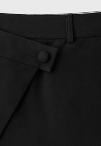 Gros plan de la ceinture d’une jupe en tissu noir avec un bouton recouvert de tissu et un passant de ceinture.