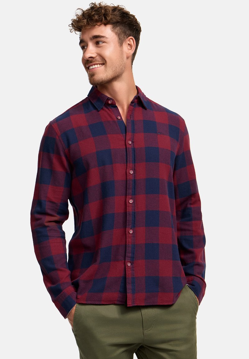 Camisa de cuadros roja y azul marino con botones, hecha de una tela de textura suave; cuenta con un collar y mangas largas, combinada con pantalones verde oliva.