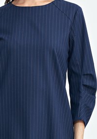 Granatowa bluzka z okrągłym dekoltem i rękawami o długości trzech czwarte, z pionowymi białymi prążkami oraz gładką, fakturowaną tkaniną.