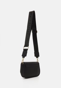 Černá kožená crossbody taška s texturovaným povrchem, která má zlatou sponu a široký popruh s nápisem "VALENTINO" v černé barvě.