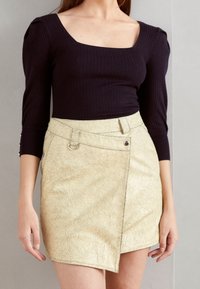 Schwarzes, geripptes Langarmoberteil mit quadratischem Ausschnitt, kombiniert mit einem beigefarbenen Minirock aus genarbtem Leder, der seitliche Knopf- und Schlaufen-Details aufweist.