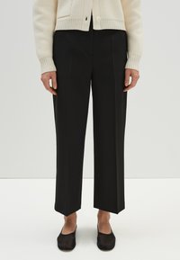 Zwarte wijde broek met een getailleerde pasvorm, voorzien van een rechte zoom en een voornaad, gecombineerd met zwarte instappers.