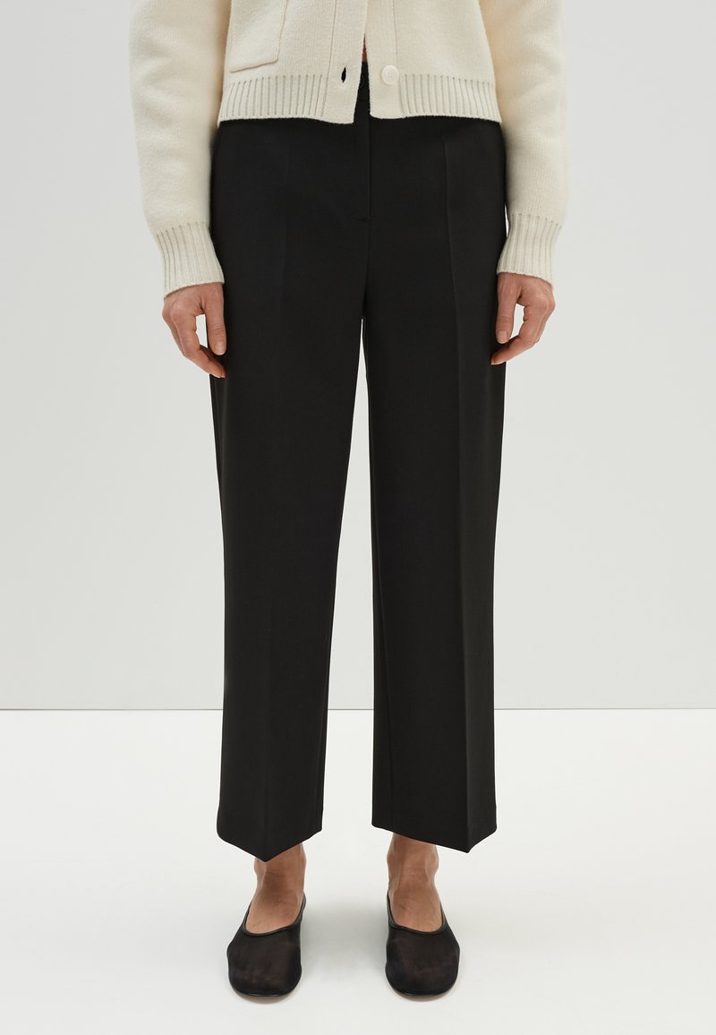 Zwarte wijde broek met een getailleerde pasvorm, voorzien van een rechte zoom en een voornaad, gecombineerd met zwarte instappers.