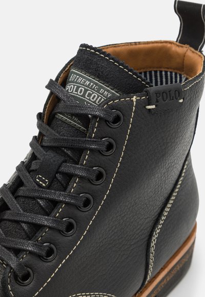 Stivale alla caviglia in pelle nera con finitura testurizzata, cuciture bianche in contrasto, punta rotonda e design con lacci, dotato di colletto imbottito e etichetta con logo.