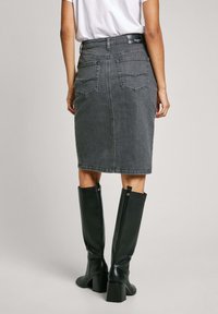 Siva denim oljnica s hrbtnimi žepi, kombinirana z črnimi usnjenimi škornji do kolen, ki imajo širok pete in zlate detajle.