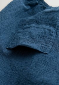 Donkerblauwe gestructureerde stof met een opgestikte zak. Het gekreukte oppervlak wijst op een lichtgewicht materiaal, wat het casual uiterlijk versterkt.