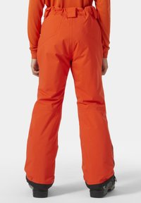 Světlé oranžové lyžařské kalhoty s volným střihem, elastickým pasem a zesílenými manžetami. Vyrobené z voděodolného materiálu, vhodné pro zimní sporty.