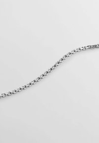 Cadena de metal plateado con eslabones circulares entrelazados y un acabado pulido, situada sobre un fondo claro.