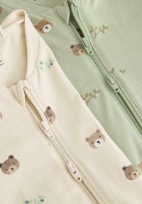 Δύο φορμάκια μωρού με φερμουάρ· το ένα εκρού με σχέδια αρκούδας, το άλλο ανοιχτό πράσινο με σχέδια αρκούδας και φυλλώματος. Μαλακό ύφασμα, φερμουάρ στο μπροστινό μέρος.