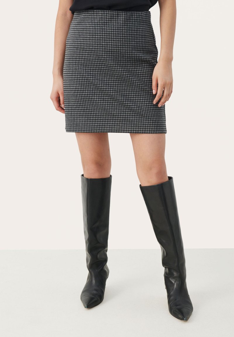 Minihame mustatavalkoinen houndstooth-kuviointi, tiukka muotoilu, suora helma ja korkea vyötärö, yhdistettynä polven yli ulottuviin mustiin nahkabootseihin.