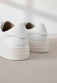 Chaussures en cuir blanc avec surface texturée, arrière arrondi et épaisse semelle en caoutchouc blanche. Les détails de couture complètent le design minimaliste.