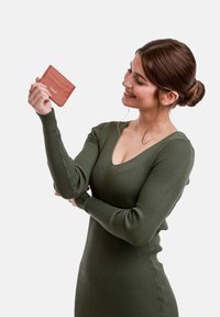 Držitel karet z rezavé kůže s texturovaným povrchem, který drží osoba v žebrovaných olivově zelených dlouhých šatech a předvádí jeho kompaktní design.