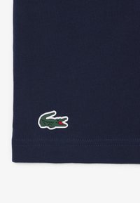 Tela azul oscuro con un pequeño logo de cocodrilo verde bordado cerca del dobladillo, cosido con hilo a juego.