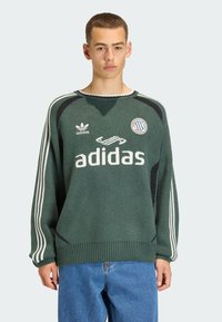 Zielony dziergany sweter z białymi i czarnymi akcentami, z okrągłym dekoltem, ściągaczem u dołu i bocznymi paskami. Widoczne jest wyraźnie logo Adidas.
