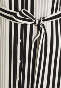 Svart-och-vit randig textil med ett knytbälte, med en knapp-down framsida och en slät yta. Ränderna varierar i tjocklek.