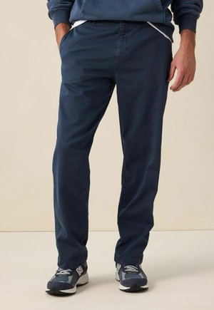 Pantalons droit bleu marine en matériau doux, dotés de poches latérales et d'un design simple, associés à des chaussures de sport grises et noires.