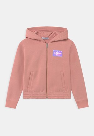 Sudadera de cremallera rosa claro, hecha de una tela suave, con una gran capucha, dos bolsillos delanteros y un parche de logo holográfico en el pecho.