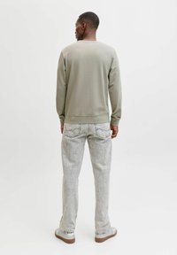 Khaki sweatshirt med rund hals og ribstrikkede manchetter, kombineret med lysegrå jeans med lommer. Modellen bærer grå sneakers.