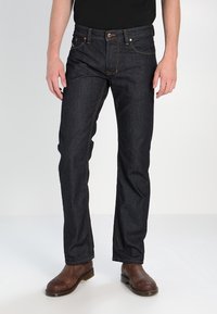 Mörkblå denimjeans med synlig sömnad, rak passform och klassisk design. Modellen bär bruna läderskor.