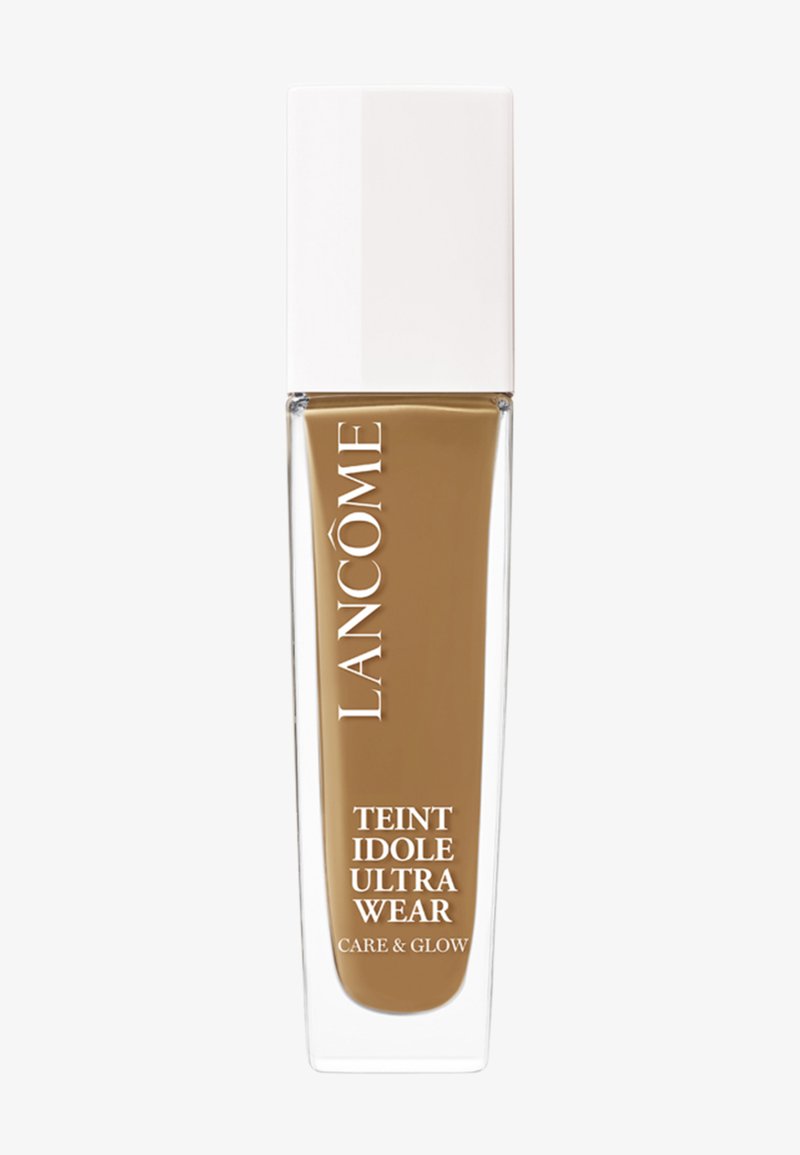 Fond de teint liquide marron dans une bouteille en verre transparent avec un capuchon blanc. L'étiquette indique "LANCÔME TEINT IDOLE ULTRA WEAR CARE & GLOW."