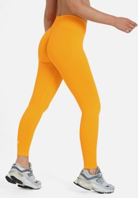 Hoog-getailleerde gele leggings met een gladde textuur, een slanke pasvorm en zijnaaddetails, gecombineerd met grijze hardloopschoenen.
