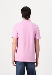 Rosa Polohemd mit Kragen, kurzen Ärmeln und geradem Saum, aus weichem Stoff. Getragen mit dunkelblauen Jeans.
