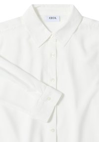Chemise blanche à col classique avec un design à boutons, présentant une fermeture à bouton en perle, une texture lisse et une étiquette "CECIL" au cou.