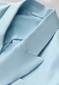 Col et revers de blazer bleu clair montrant une texture de tissu lisse et des coutures détaillées en gros plan.