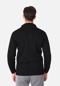 Maglione nero lavorato a maglia con finitura testurizzata, caratterizzato da un colletto alto e polsini a costine. Progettato con una vestibilità ampia e in un colore uniforme.