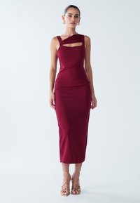 Bordo spalvos aptempta suknelė su asimetrišku dirželių dizainu ir iškirptomis priekyje prie iškirptės. Lygios tekstūros audinys, ilgis iki kelių. Auksiniai aukštakulniai su dirželiais.