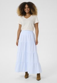 Jupe maxi rayée bleu clair et blanche avec des couches superposées, une taille élastique, associée à un t-shirt beige à col en V et des bottines brunes.