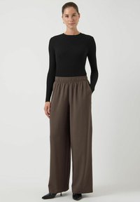 Zwart geribbeld langarmtop gecombineerd met losvallende, hoog getailleerde bruine broek. De broek heeft zijzakken en een zachte textuur.