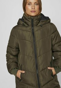 Kombinēts tumši zaļš ķermeņa mētelis ar augstu apkakli un noņemamu kapuci, ar priekšējo rāvējslēdzēju un sānu kabatām, izgatavots no gludas auduma.