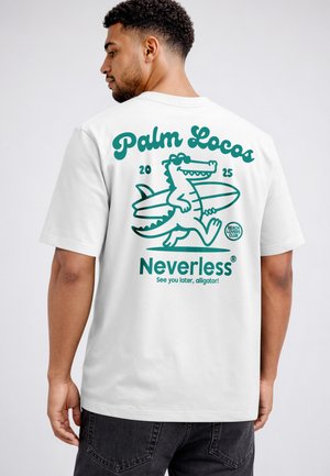 Man wearing white t-shirt with teal graphic of cartoon alligator carrying surfboard and text "Palm Locos 2025 Neverless."