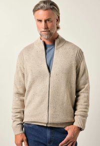 Béžový svetr na zip s ribbovaným límcem a manžetami, strukturovaná tkanina s barevnými tečkami, nošený přes modré tričko.