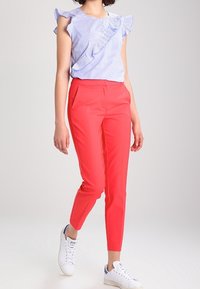 Blouse rayée bleue et blanche avec des manches volantées, associée à un pantalon rouge ajusté et des baskets blanches. Design simple et moderne.