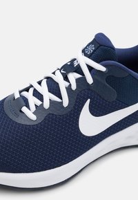 Zapatilla deportiva azul marino con cordones blancos, parte superior de malla texturizada, diseño estilizado y un destacado logo blanco de Nike en el lateral.