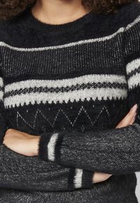 Svart och grå stickad tröja med rund halsringning, med randiga mönster och geometriska former. Mjuk textur, långa ärmar med accentstripes.