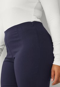 Pantaloni aderenti blu navy realizzati in un tessuto morbido, con cerniera sul retro, vita stretta e design slanciato con sottili dettagli di cucitura.