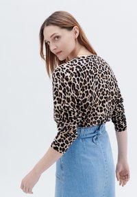 Leopardmönstrad långärmad tröja med åtsittande manschetter, kombinerad med en högmidjad ljusblå denimkjol med knytmidja.