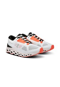 Baskets de course blanches avec des lacets noirs et des accents orange. Tige en mesh pour la respirabilité, semelle rembourrée avec un design perforé pour le confort.