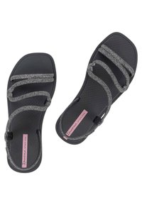 Sandali neri con una suola testurizzata e tre cinghie brillanti. Presentano un'etichetta rosa con la scritta "Ipanema sempre nova". Design piatto.