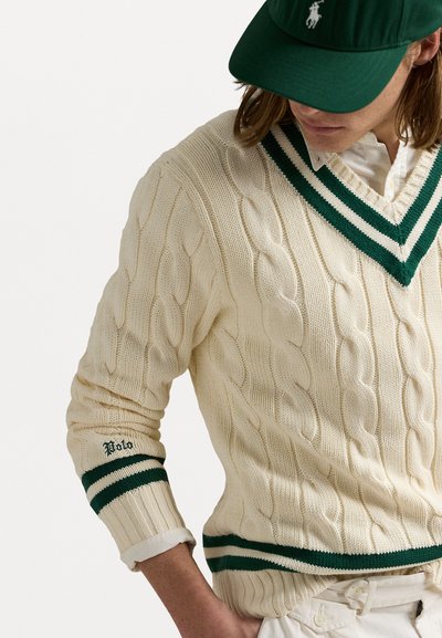 Creme kabelstrik sweater med V-hals, grønne striber på kraven og manchetterne, med "Polo" broderet på ærmet.