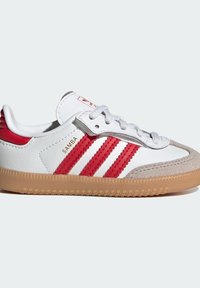 White leather sneaker with red stripes, grey suede toe, and textured gum rubber sole. Features white laces and branding on the tongue.