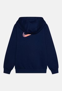 Námořnická modrá mikina s kapucí, měkké textury, s růžově přecházejícím logem Nike na zadní straně. Obsahuje přední kapsu a nastavitelnou šňůrku na kapuci.